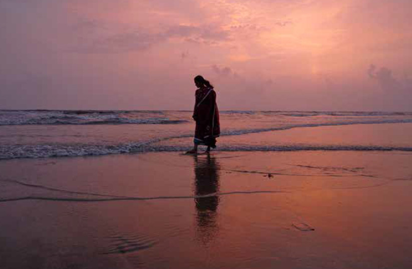 A WOMAN walks along the beach in Mumbai as the sun sets. (photo credit: VIVEK PRAKASH/REUTERS)