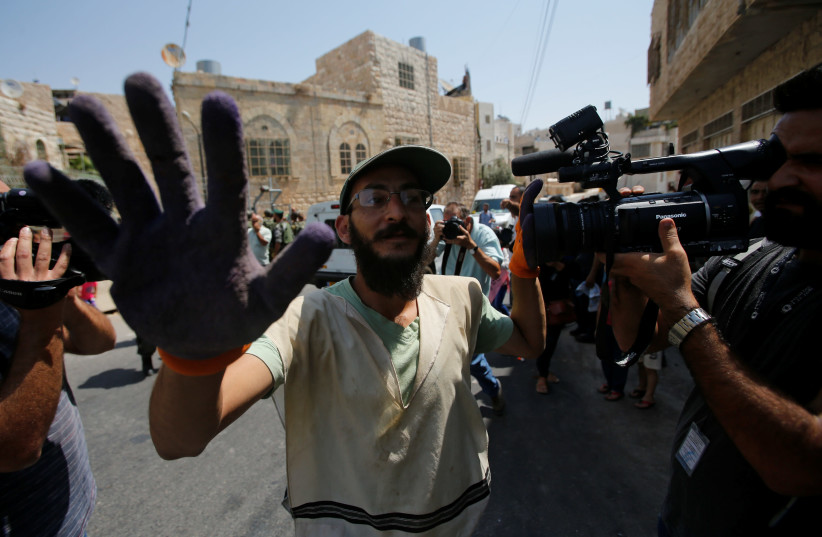 An Israeli settler blocks cameras during a protest by Palestinians in the old city of the West Bank city of Hebron, September 3, 2017 (photo credit: MUSSA QAWASMA / REUTERS)