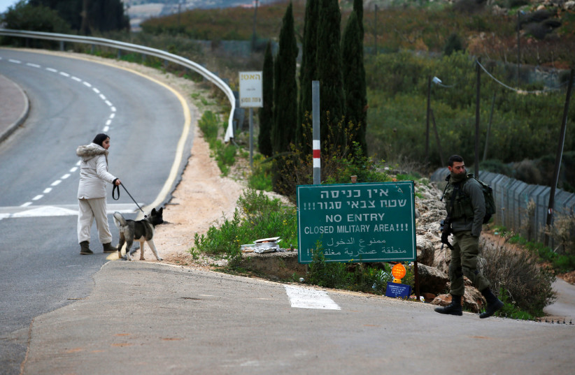 A woman walks her dog as an Israeli soldier guards near the border with Lebanon, the morning after the Israeli military said it had launched an operation to "expose and thwart" cross-border attack tunnels from Lebanon, in Israel's northernmost town Metula December 5, 2018 (photo credit: REUTERS/Ronen Zvulun)