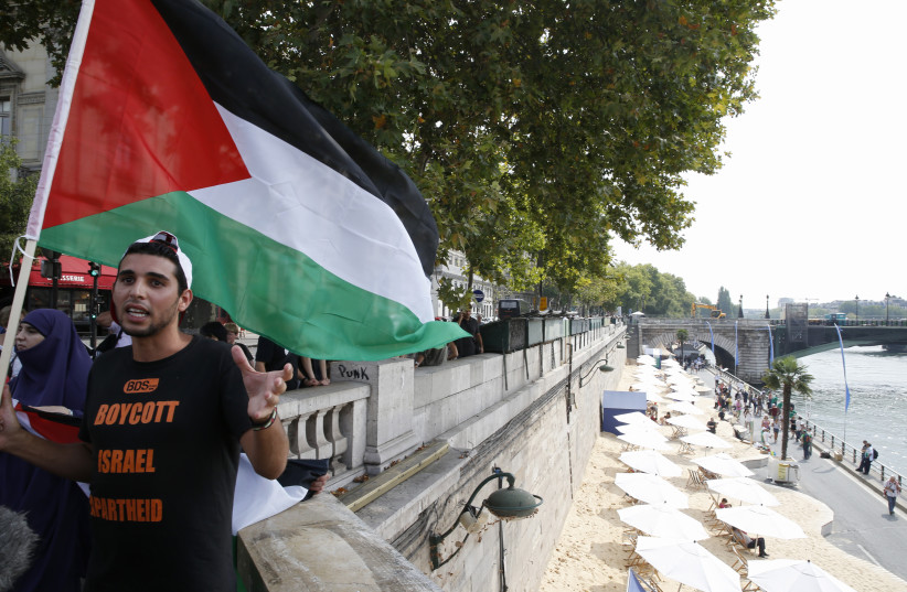 A man wearng a T-shirt with the message, ''Boycott Israel Apartheid'' holds a Palestinian flag during a protest action on a bridge overlooking umbrellas placed along the artificial beach along the ''Paris Plages'' event, in Paris, France, August 13, 2015. Paris' decision to celebrate ''Tel Aviv on Seine'' (credit: REUTERS/PASCAL ROSSIGNOL)