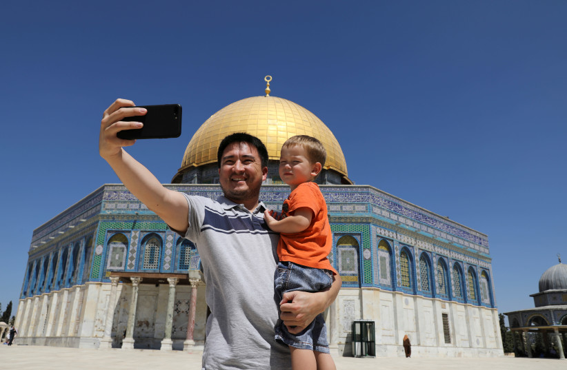 A Muslim tourist holds a child as he takes a selfie photo in front of the Dome of the Rock on the compound known to Muslims as Noble Sanctuary and to Jews as Temple Mount, in Jerusalem's Old City August 31, 2017 (photo credit: REUTERS/AMMAR AWAD)
