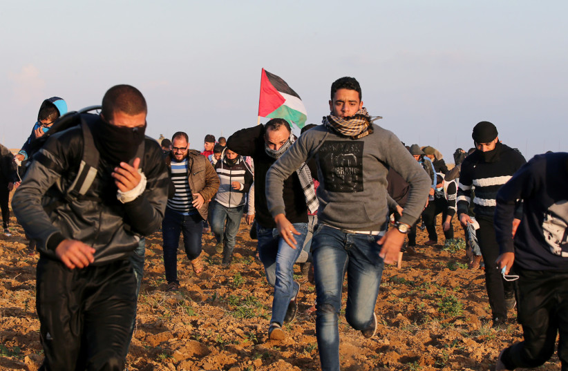 Palestinian demonstrators run for cover from Israeli gunfire and tear gas during a protest near the Israel-Gaza border fence, in the southern Gaza Strip December 21, 2018 (photo credit: IBRAHEEM ABU MUSTAFA / REUTERS)
