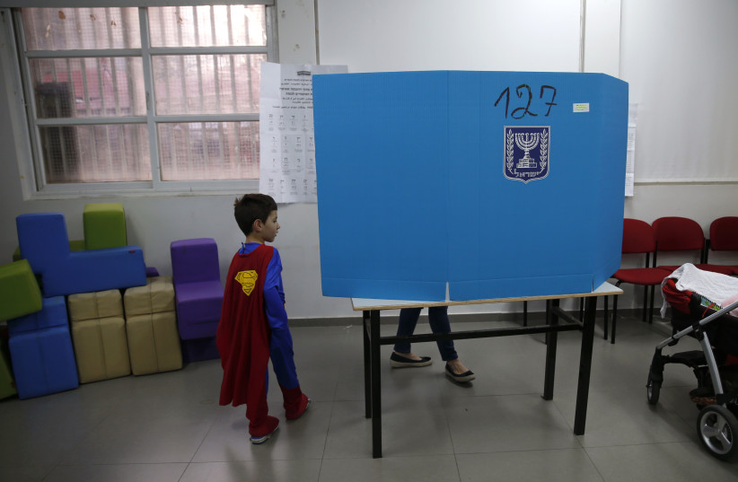 An Israeli boy, dressed in a Superman costume, escorts his mother behind a voting booth at a polling station in Tel Aviv March 17, 2015 (photo credit: BAZ RATNER/REUTERS)