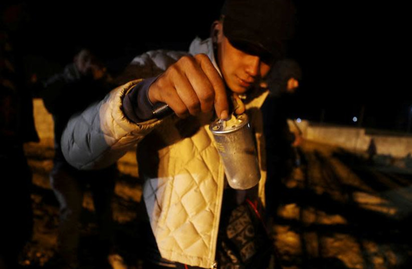 A migrant, part of a caravan of thousands from Central America trying to reach the United States, holds a tear gas canister after U.S. Customs and Border Protection (CBP) officials threw it to the Mexican side of the fence as migrants prepare to cross it illegally, in Tijuana, Mexico, January 1, 201 (photo credit: REUTERS/MOHAMMED SALEM)