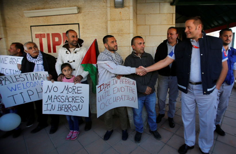 A Palestinian man shakes hands with a member of the Temporary International Presence in Hebron (TIPH) during a protest against Israeli Prime Minister Benjamin Netanyahu's decision not to renew the mandate of TIPH, in Hebron. January 30, 2019. (photo credit: MUSSA QAWASMA/REUTERS)