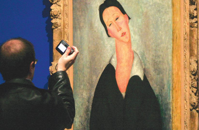 A man photographs a painting entitled ‘Portrait de femme polonaise’ (Portrait of a Polish woman) painted in 1919 by Italian Jewish artist Amedeo Modigliani, at the Thyssen-Bornemisza Museum in Madrid (photo credit: PAUL HANNA/REUTERS)