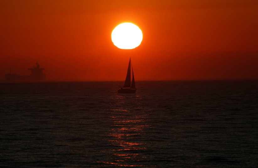 The sun sets behind a yacht crossing through the Straits of Gibraltar, off the British overseas territory of Gibraltar December 6, 2018. (photo credit: DARRIN ZAMMIT LUPI/REUTERS)