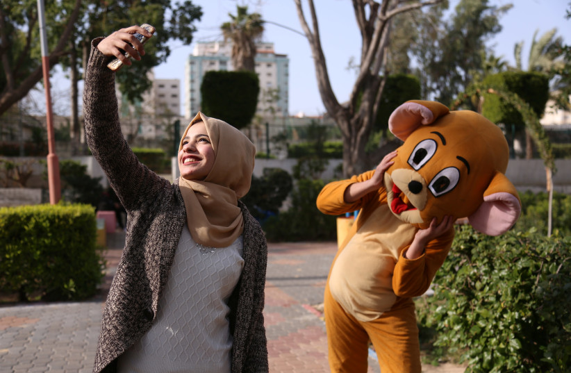 Palestinian high school student Wessal Abu Amra, 17, takes a selfie with a person wearing a costume at a public park in Gaza City, February 14, 2019. (photo credit: SAMAR ABO ELOUF / REUTERS)