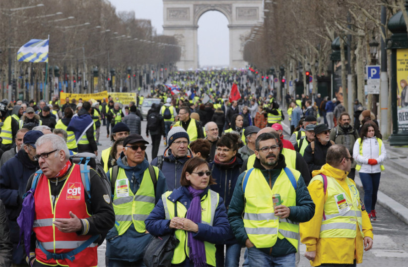 Protesters wearing yellow vests walk down the Champs Elysees in Paris on March 9 (photo credit: PHILIPPE WOJAZER / REUTERS)