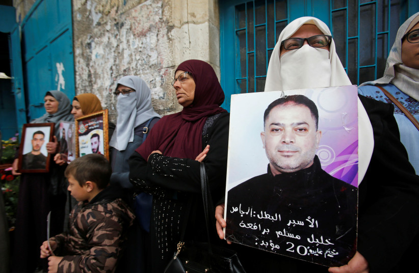 A woman holds a picture of a Palestinian prisoner held in an Israeli jail, during a rally marking Palestinian Prisoners' Day, in Bethlehem in the Israeli occupied West Bank April 17, 2019 (photo credit: MUSSA QAWASMA / REUTERS)