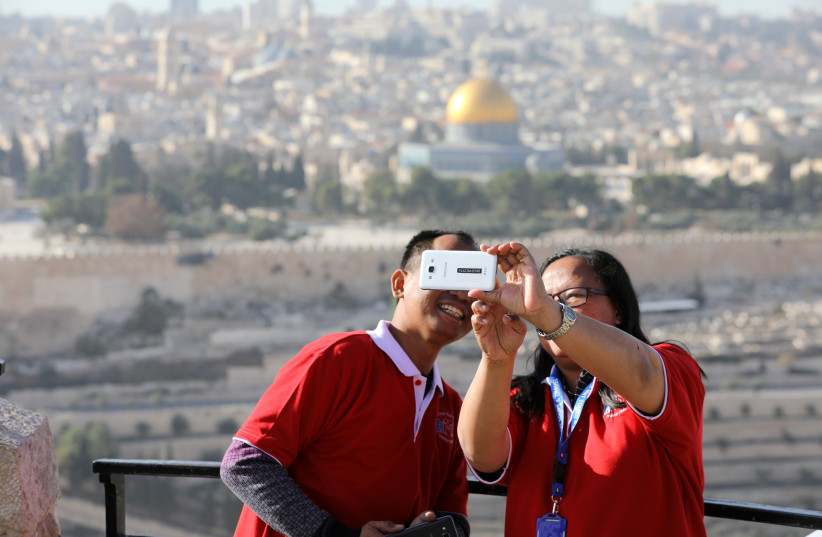Tourists look at a mobile phone as they stand at an observation point overlooking the Dome of the Rock and Jerusalem's Old City December 10, 2017. Picture taken December 10, 2017 (photo credit: AMMAR AWAD / REUTERS)