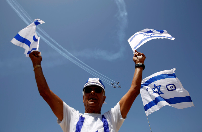 A man waves flags of Israel as Israeli Air Force planes fly in formation over the Mediterranean Sea during an aerial show as part of the celebrations for Israel's Independence Day marking the 70th anniversary of the creation of the state, in Tel Aviv, Israel April 19, 2018. (photo credit: REUTERS/AMIR COHEN)