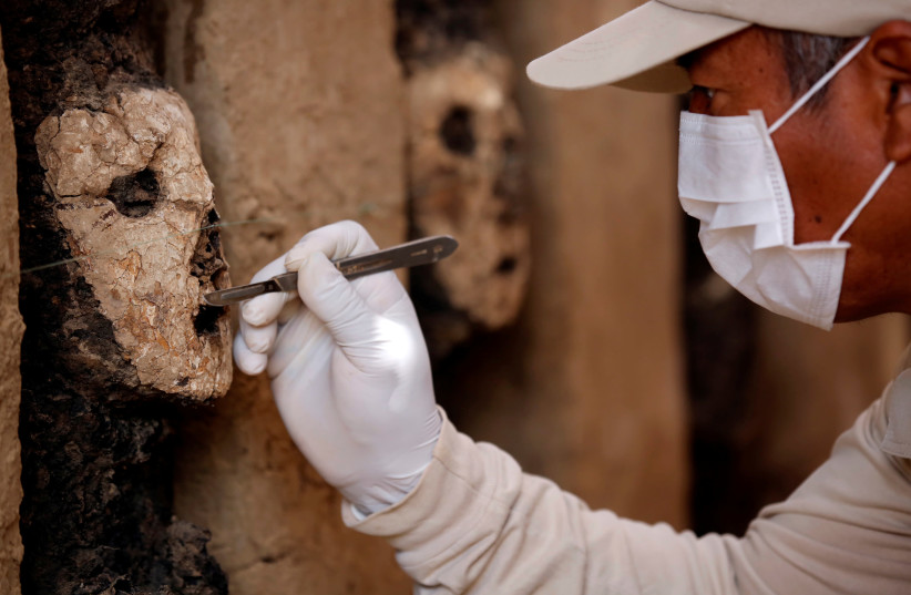 An archaeologist cleans a wooden mask of the Mochica culture at Chan Chan archeological complex in Trujillo, Peru October 22, 2018. (photo credit: DOUGLAS JUAREZ / REUTERS)