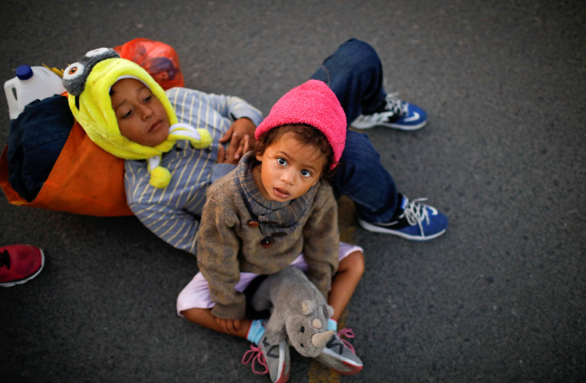 Children, belonging to a caravan of migrants from Honduras en route to the United States, wait with their parents at the border bridge in Tecun Uman (photo credit: JOSE CABEZAS/REUTERS)
