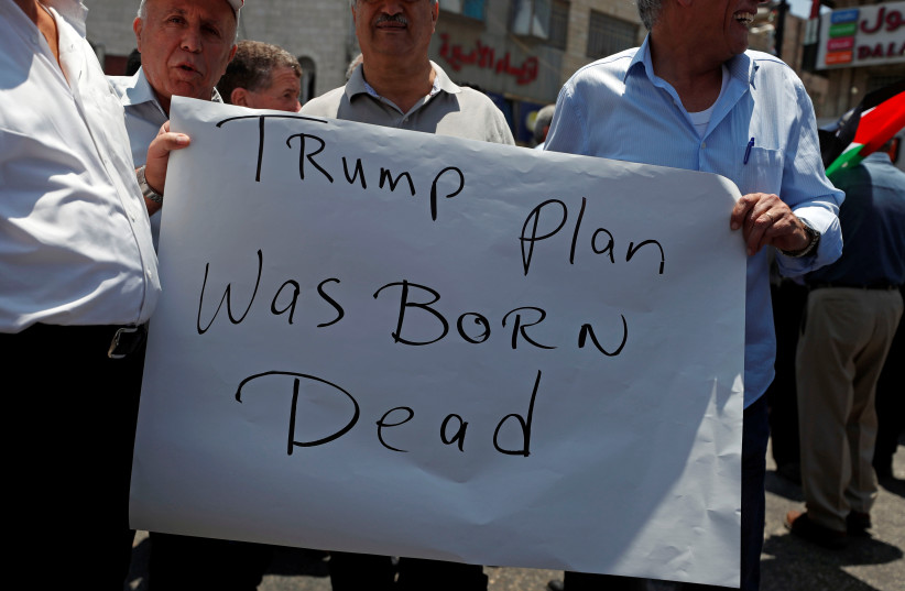 Palestinians hold a sign during a protest against the U.S.-led economic workshop for Mideast plan that is hosted by Bahrain, in Ramallah in the Israeli occupied West Bank, June 15, 2019 (photo credit: MOHAMAD TOROKMAN/REUTERS)