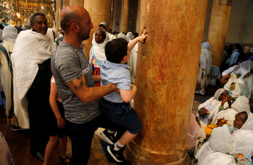 A boy is carried as he places his fingers inside holes in a column that form the shape of a cross at the Church of the Nativity in Bethlehem, in the West Bank April 27, 2019. (photo credit: RANEEN SAWAFTA/ REUTERS)