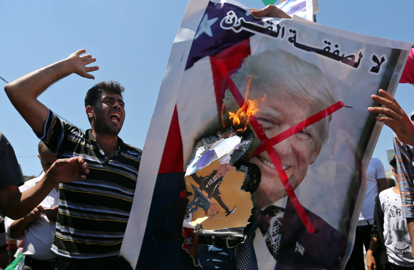 Palestinian demonstrators burn a crossed-out poster depicting U.S. President Donald Trump and reading: "no for Deal of the Century" during a protest against Bahrain's workshop for U.S. Middle East peace plan, in the southern Gaza Strip, June 26, 2019 (photo credit: IBRAHEEM ABU MUSTAFA / REUTERS)