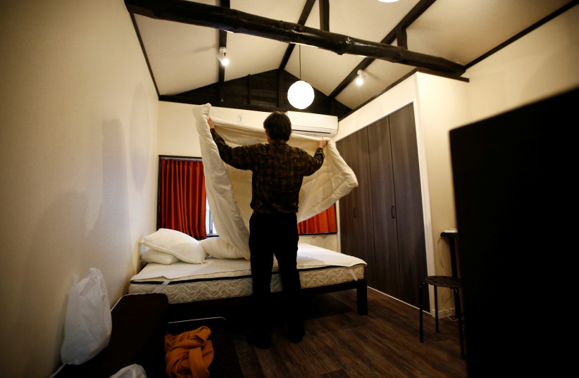 Yasuhiro Inaoka, who manages apartments for owners who provide short-term homestay lodging, arranges a bed after guests checked out at an apartment which is used as Airbnb service in Tokyo (credit: REUTERS)