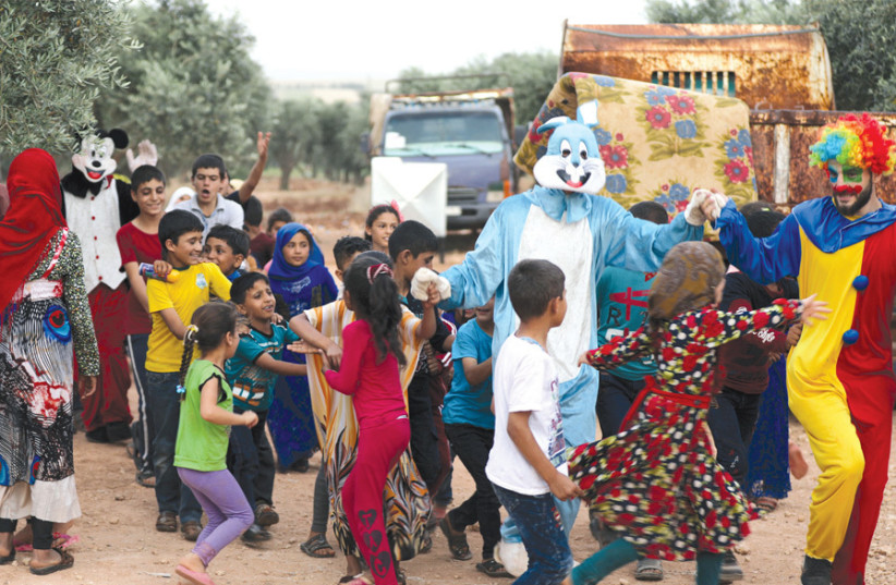 A CLOWN and cartoon characters entertain displaced Syrian refugee children during the Muslim holiday of Eid al- Fitr, in an olive grove in Syria’s Idlib countryside on June 4. (photo credit: KHALIL ASHAWI / REUTERS)