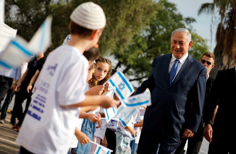 Israeli Prime Minister Benjamin Netanyahu greets students as they wave Israeli flags during a ceremony opening the school year in the settlement of Elkana on September 1, 2019.  (photo credit: REUTERS/AMIR COHEN)