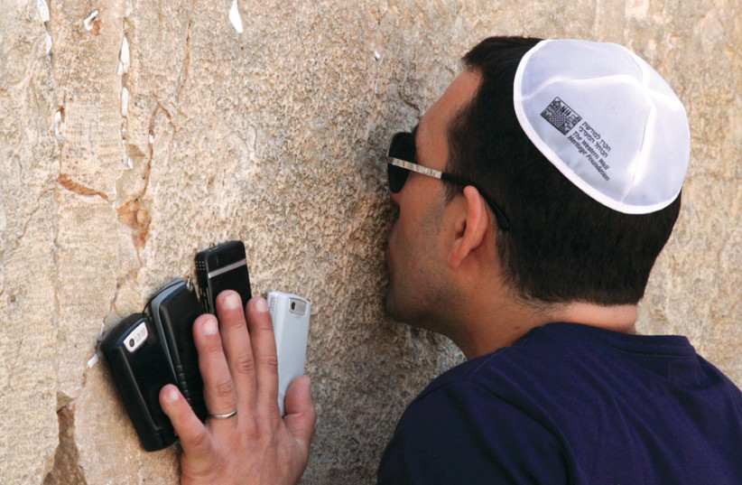 A visitor prays at the Western Wall, holding four cellphones (photo credit: MARC ISRAEL SELLEM)
