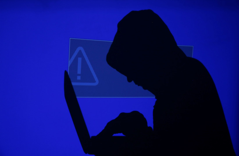 Hooded man holds laptop computer as blue screen with an exclamation mark is projected on him (photo credit: REUTERS/KACPER PEMPEL)