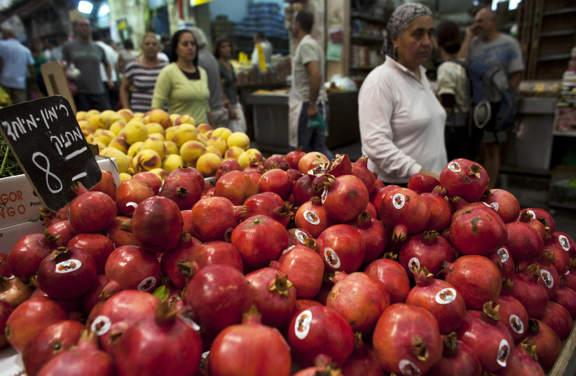 Israelis walk past a shop selling pomegranates in Mahne Yehuda Market in central Jerusalem, ahead of Rosh Hashana (photo credit: REUTERS)
