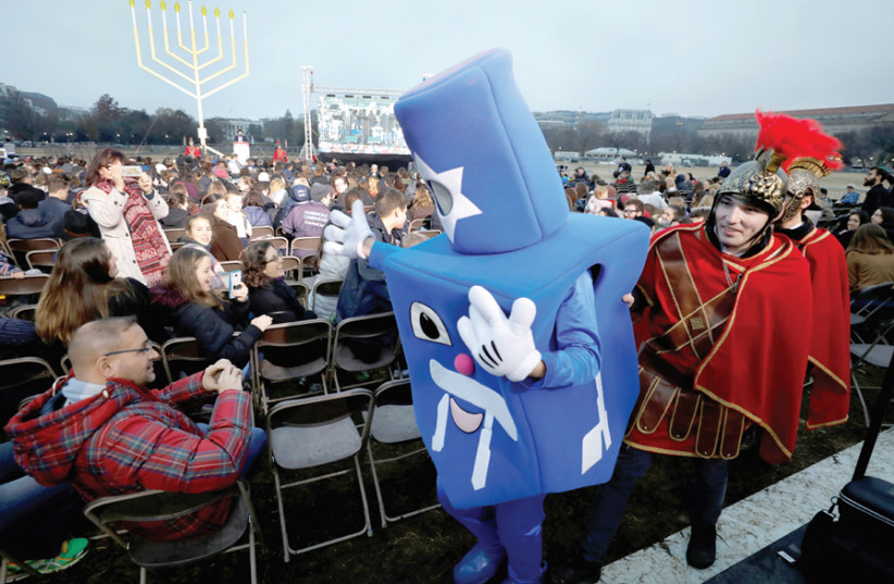 PITCHES TO Jews in America about their practice are diverse – Dreidel Man is escorted by Maccabee-costumed men before the National Menorah ceremony to mark Hanukkah near the White House, December 2018. (photo credit: YURI GRIPAS / REUTERS)
