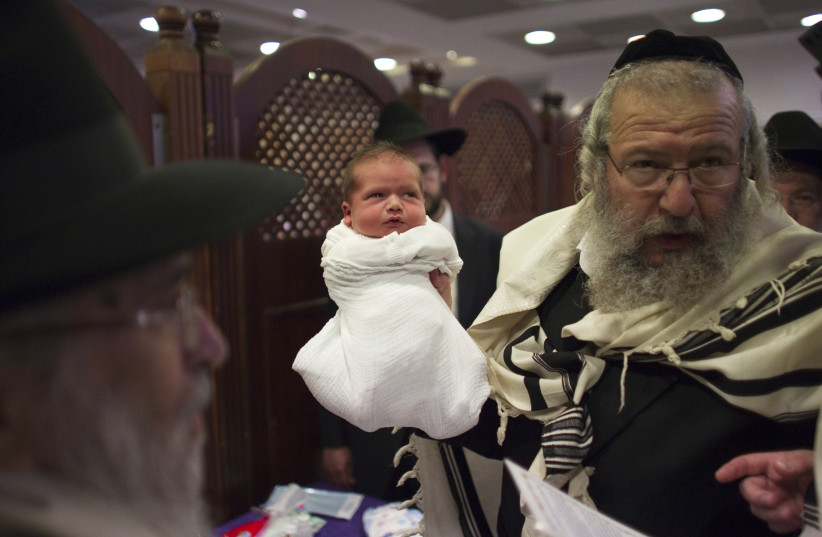 Rabbi Moshe Wiseberg, a "mohel", or ritual circumciser, holds a baby after circumcising him in Jerusalem (photo credit: REUTERS/Ronen Zvulun)