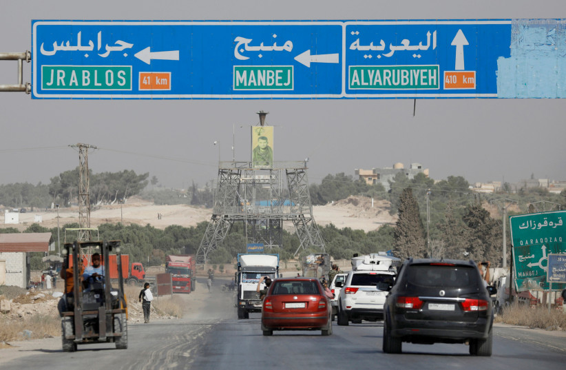 Cars pass under a road sign that shows the direction to Manbij city, at the entrance of Manbij, Syria (photo credit: REUTERS/OMAR SANADIKI)