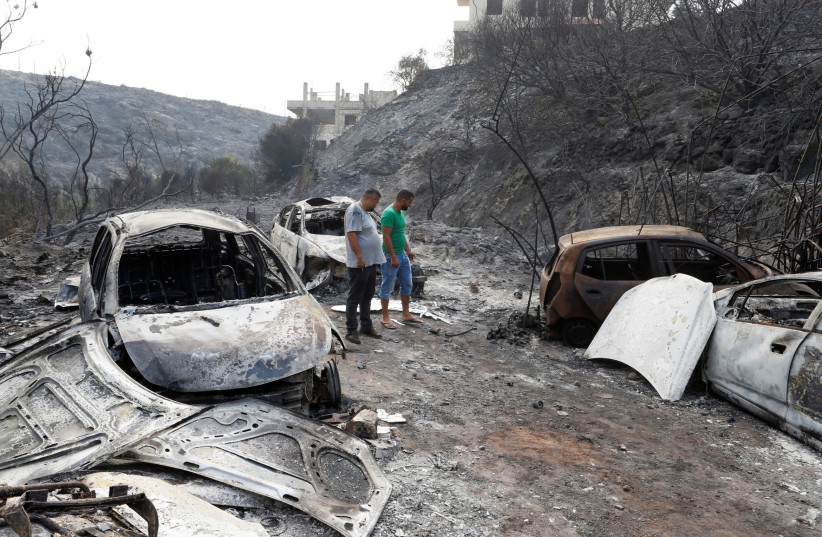 People look at burned vehicles after wildfires swept through Damour, south of Beirut, Lebanon October 15, 2019 (photo credit: MOHAMED AZAKIR / REUTERS)