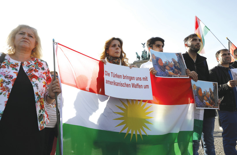 PROTESTERS HOLD PICTURES and Kurdish flags during a rally against the Turkish military operation in Syria, in Berlin, this week. The sign reads: ‘The Turks murder us with American weapons.’  (photo credit: MICHELE TANTUSSI / REUTERS)