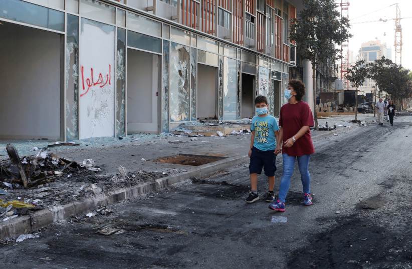 People wearing masks walk past damaged shops, a day after protests targeting the government over an economic crisis in Beirut, Lebanon October 19, 2019 (photo credit: REUTERS/MOHAMED AZAKIR)