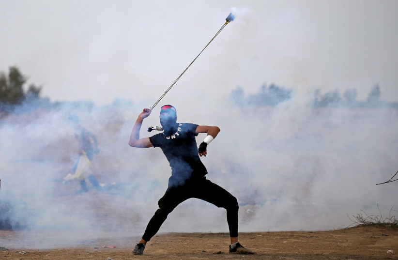 A Palestinian demonstrator uses a sling to hurl back a tear gas canister during an anti-Israel protest at the Israel-Gaza border fence in the southern Gaza Strip October 25, 2019 (photo credit: REUTERS/IBRAHEEM ABU MUSTAFA)