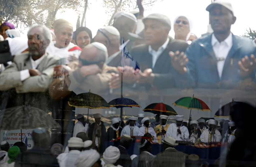 Members of the Israeli Ethiopian community are seen through a glass panel as others are reflected (bottom) in the panel during a ceremony marking the Ethiopian Jewish holiday of Sigd in Jerusalem November 7, 2018 (photo credit: AMIR COHEN/REUTERS)