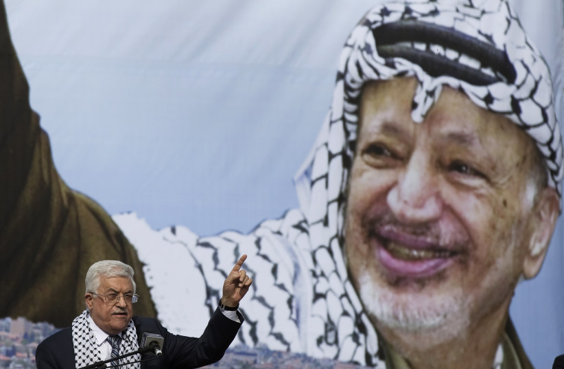 Palestinian President Mahmoud Abbas gestures beneath a poster of the late Palestinian leader Yasser Arafat (photo credit: FINBARR O'REILLY / REUTERS)