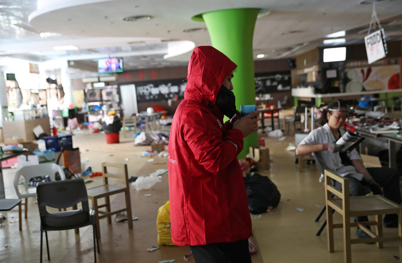 A PolyU student drinks coffee and watches the news in a canteen in Hong Kong Polytechnic University (PolyU) in Hong Kong, China November 23, 2019 (photo credit: REUTERS/LEAH MILLIS)