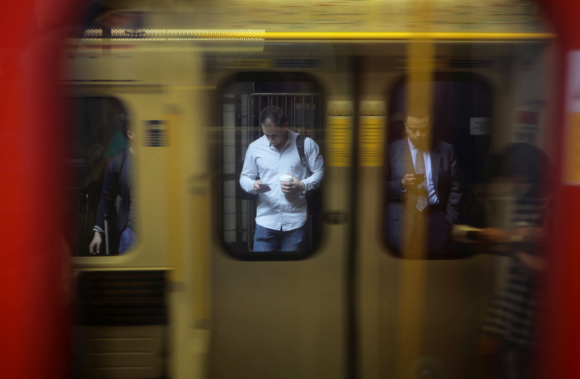 Men look at their phones at the underground platform in London (photo credit: REUTERS/KEVIN COOMBS)