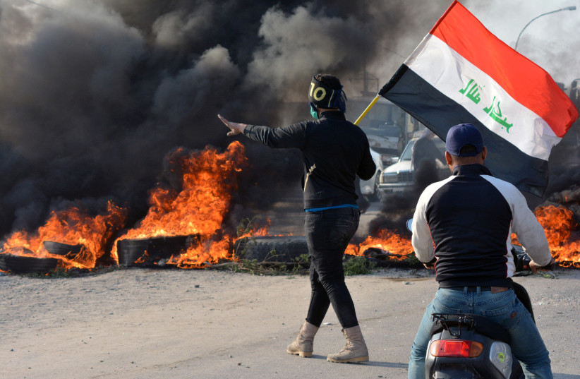 A demonstrator holds an Iraqi flag near burning tires during ongoing anti-government protests in Nassiriya, Iraq November 24, 2019 (credit: REUTERS/AHMED DHAHI)