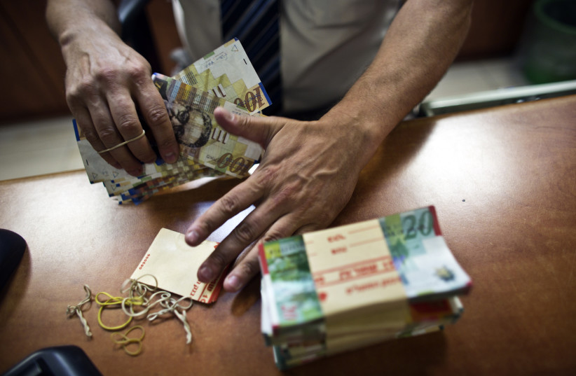 A bank employee counts Israeli Shekel notes for the camera at a bank branch in Tel Aviv (photo credit: NIR ELIAS / REUTERS)