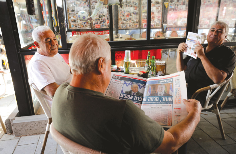 A man in a coffee shop in Ashkelon reads newspaper coverage of the prime minister's indictment last week.  (photo credit: AMIR COHEN/REUTERS)