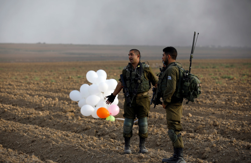 Israeli soldiers stand next to balloons in a field near the border fence between Israel and the Gaza Strip (photo credit: AMIR COHEN/REUTERS)