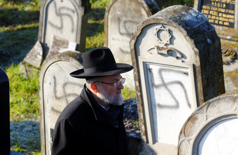 A man walks past graves desecrated with swastikas at the Jewish cemetery in Westhoffen, near Strasbourg, France, December 4, 2019.  (photo credit: ARND WIEGMANN / REUTERS)