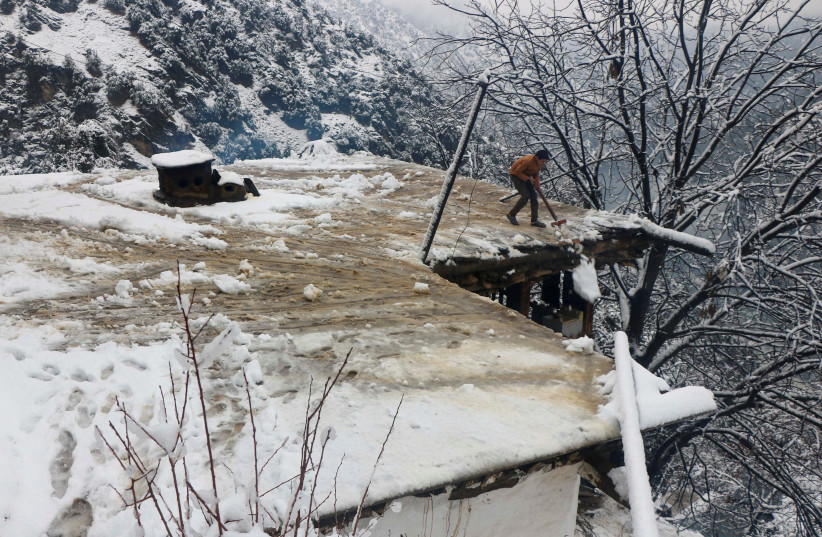 A boy clears a snow-covered roof of his family house after a heavy snowfall in Neelum Valley near line of control (LoC), Pakistan, January 13, 2020. (photo credit: REUTERS)