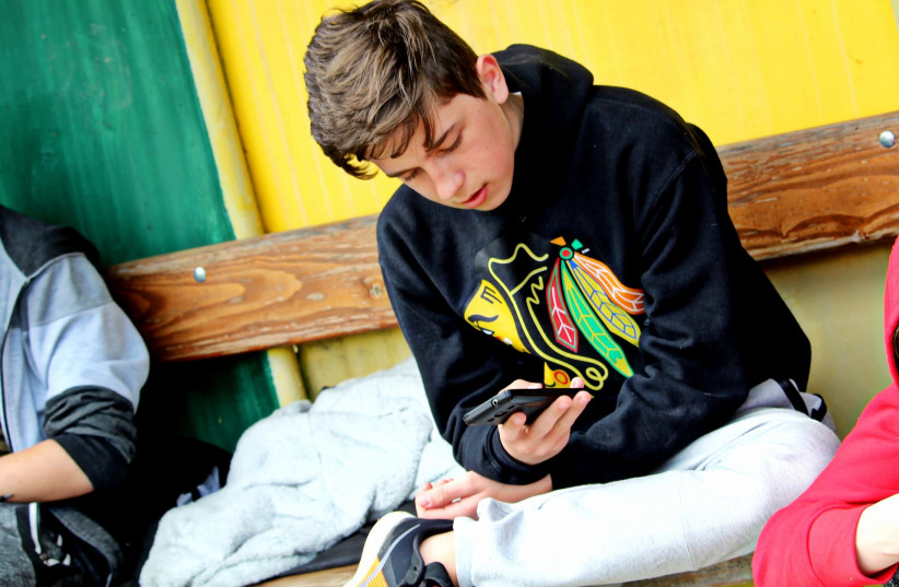 A teenage boy looks at his smartphone screen.  (photo credit: CREATIVE COMMONS)