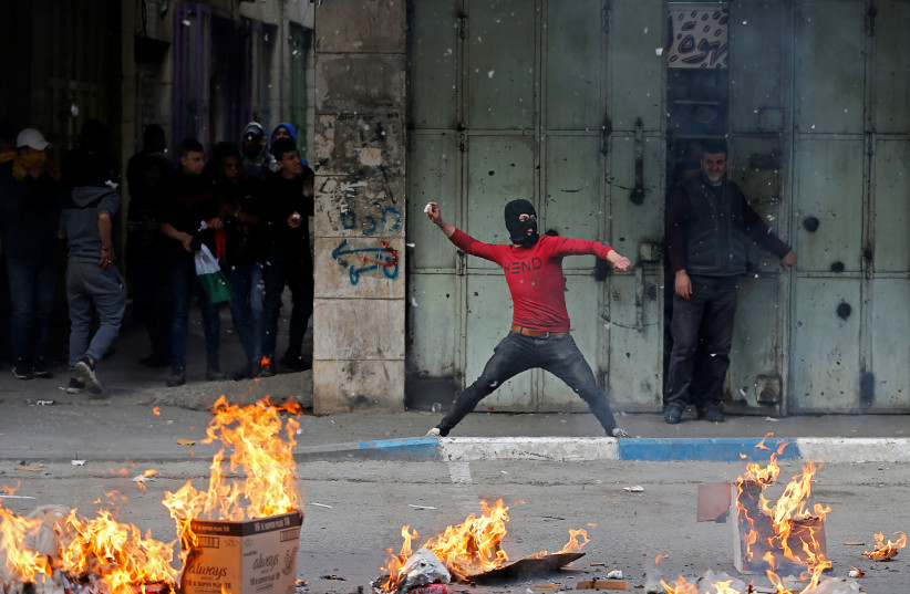A Palestinian hurls stones at Israeli troops during a protest against the U.S. President Donald Trump’s Middle East peace plan, in Hebron in the Israeli-occupied West Bank February 6, 2020 (photo credit: MUSSA QAWASMA/REUTERS)