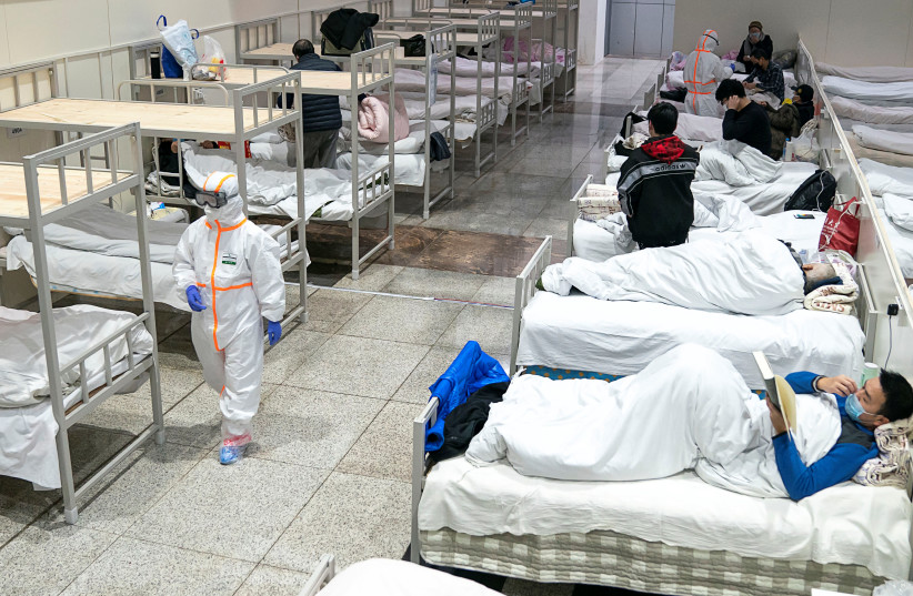 Medical workers in protective suits attend to patients at the Wuhan International Conference and Exhibition Center, which has been converted into a makeshift hospital to receive patients with mild symptoms caused by the novel coronavirus, in Wuhan, Hubei province, China February 5, 2020 (photo credit: CHINA DAILY VIA REUTERS)