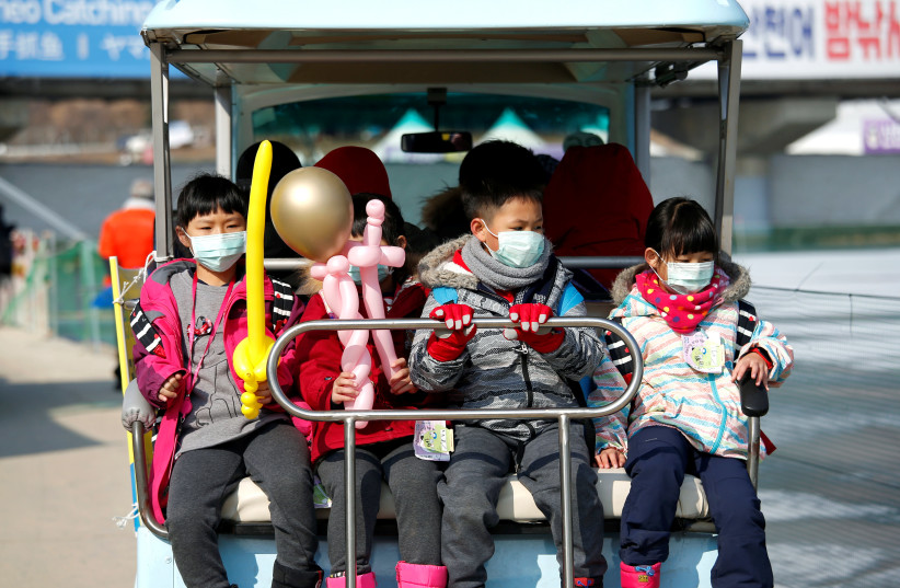 Children wearing masks to prevent contacting a new coronavirus are seen during the Ice Festival in Hwacheon, south of the demilitarized zone (DMZ) separating the two Koreas, South Korea, February 8, 2020 (photo credit: REUTERS/HEO RAN)