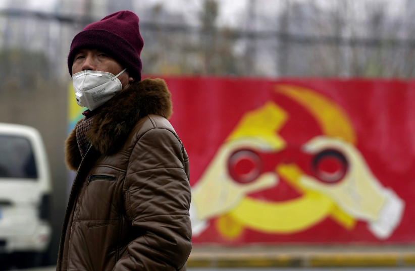 A man wears a mask as he walks past a mural showing a modified image of the Chinese Communist Party emblem in Shanghai, China after the country is hit by an outbreak of the new coronavirus, January 28, 2020 (photo credit: REUTERS/ALY SONG)
