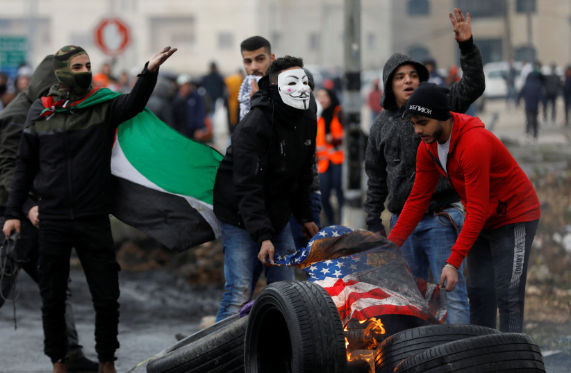 Palestinian demonstrators burn a U.S. flag during a protest against the U.S. President Donald Trump's Middle East peace plan and in support of President Mahmoud Abbas, near the Jewish settlement of Beit El in the Israeli-occupied West Bank February 11, 2020 (photo credit: REUTERS/MOHAMAD TOROKMAN)